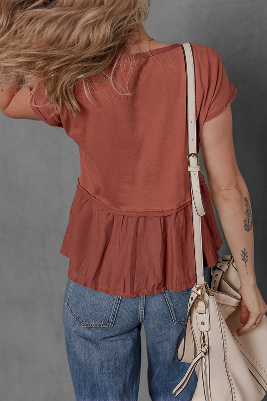 Person wearing a rust-colored peplum top and blue jeans, holding a beige handbag against a gray background.