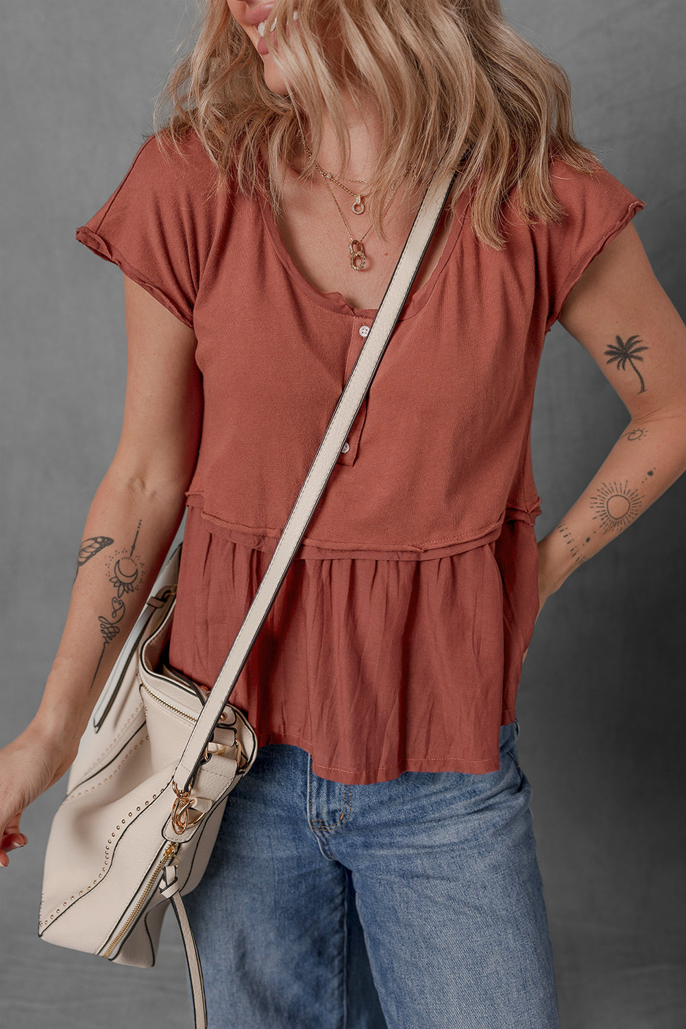 Person wearing a rust-colored top and blue jeans, holding a beige bag against a gray background