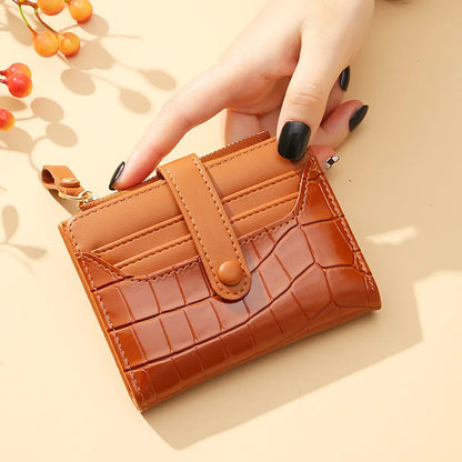 Brown textured wallet held by a hand with black nail polish on a beige background